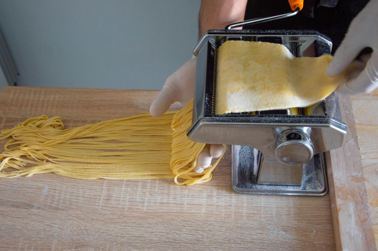 person rolling out fresh pasta from a machine