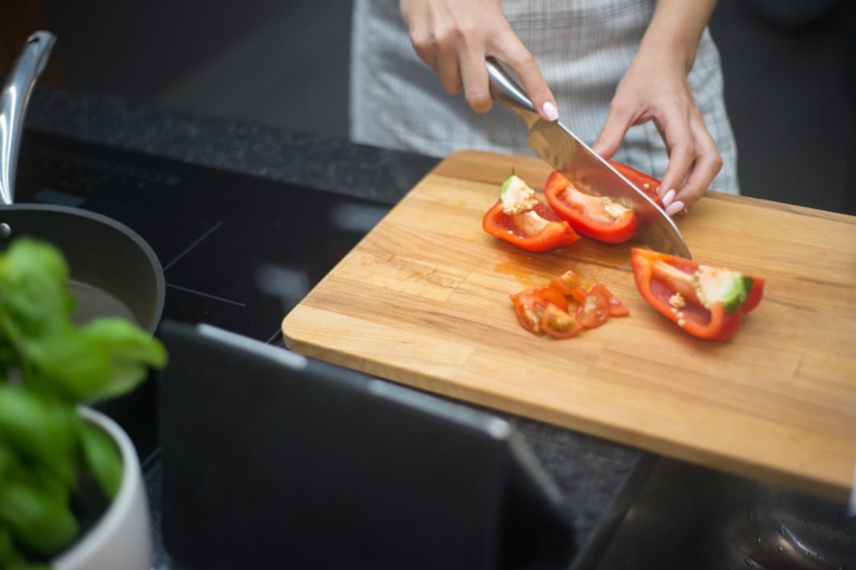 A chef demonstrating proper knife technique while slicing vegetables on a wooden cutting board
